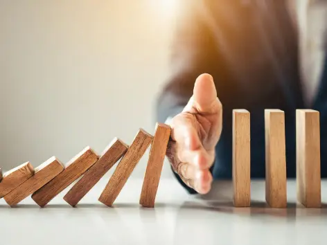 Symbolbild für Business Continuity Management (BCM): Eine Hand stoppt eine Reihe fallender Dominosteine und verhindert so eine unkontrollierte Kettenreaktion – stellvertretend für die Aufrechterhaltung der Geschäftskontinuität.